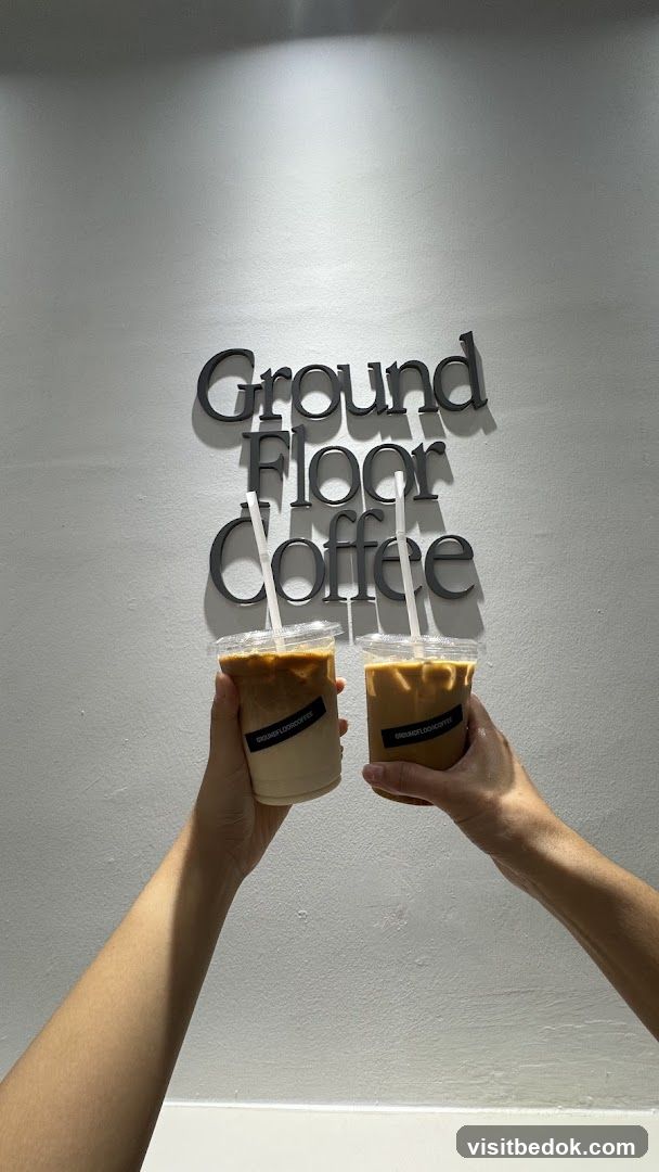 Two iced coffees held up in front of a wall with the words "Ground Floor Coffee"