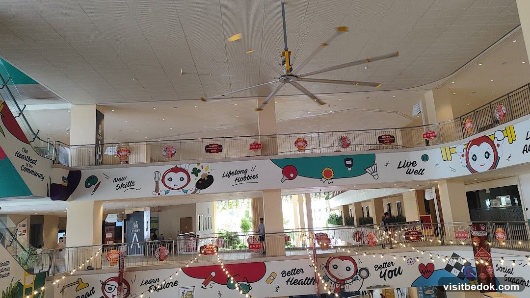Interior of a multi-level community center with decorative banners and a large ceiling fan.