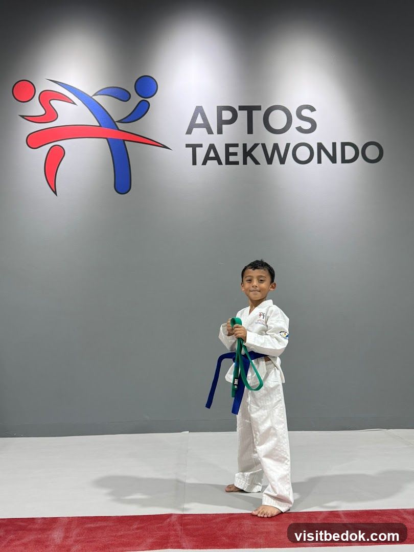 Young Taekwondo Student Poses in Front of Aptos Taekwondo Logo