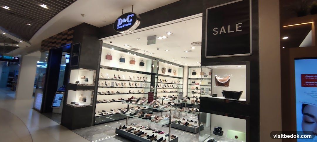 The exterior of a shoe and handbag store. The store has a large display window showcasing various shoes and handbags. A prominent sign above the entrance reads "D&C Shoes & Comfort". A "SALE" sign is displayed on the right side of the storefront.