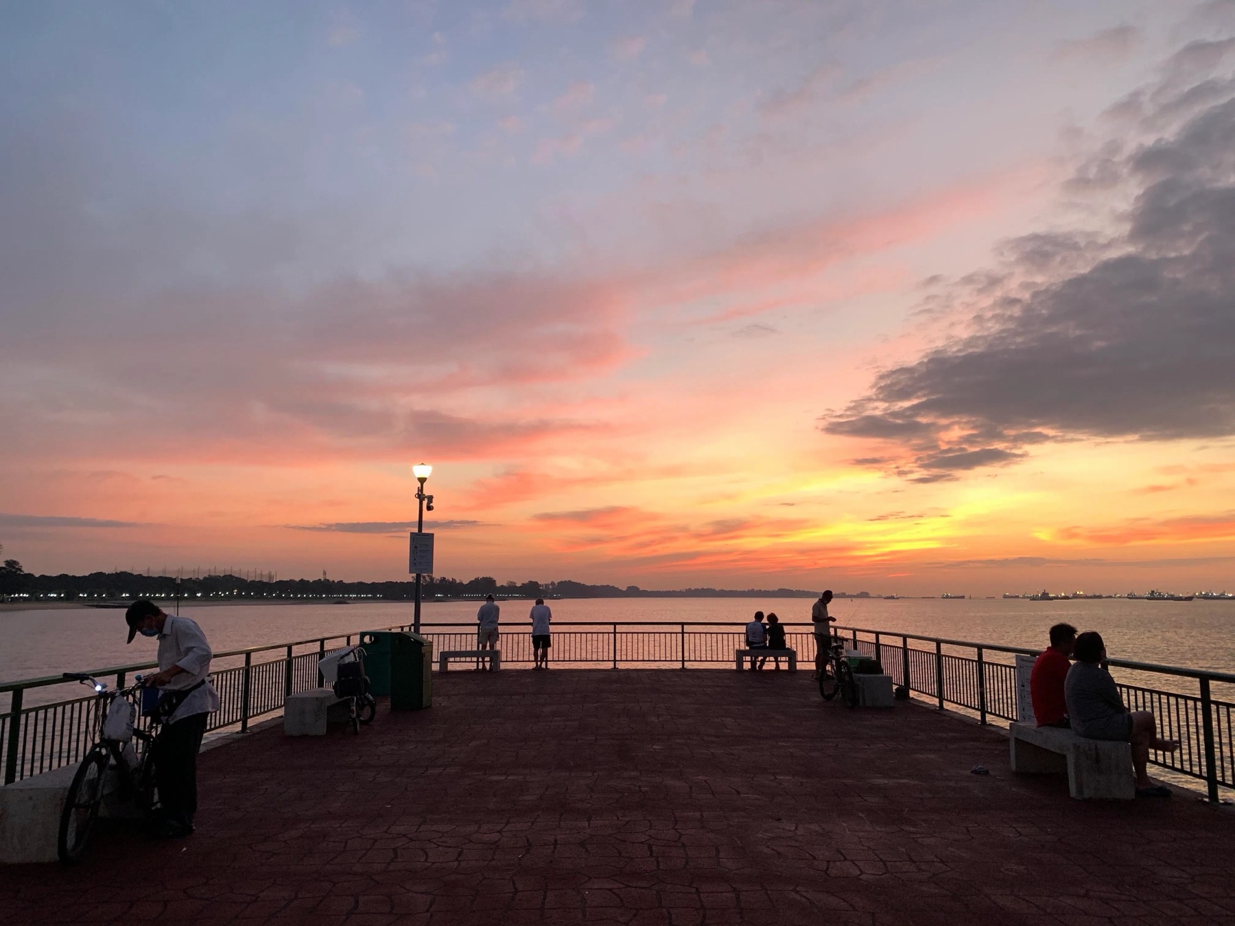 Dawn at the end of Bedok Jetty in East Coast Park Area F, with people and bicycles along the green rail