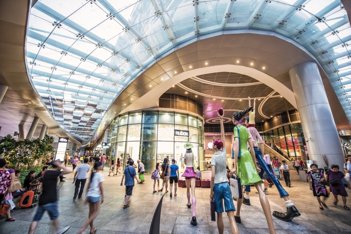 Bedok Mall atrium with glass canopy, family sculptures, and shoppers on the concourse