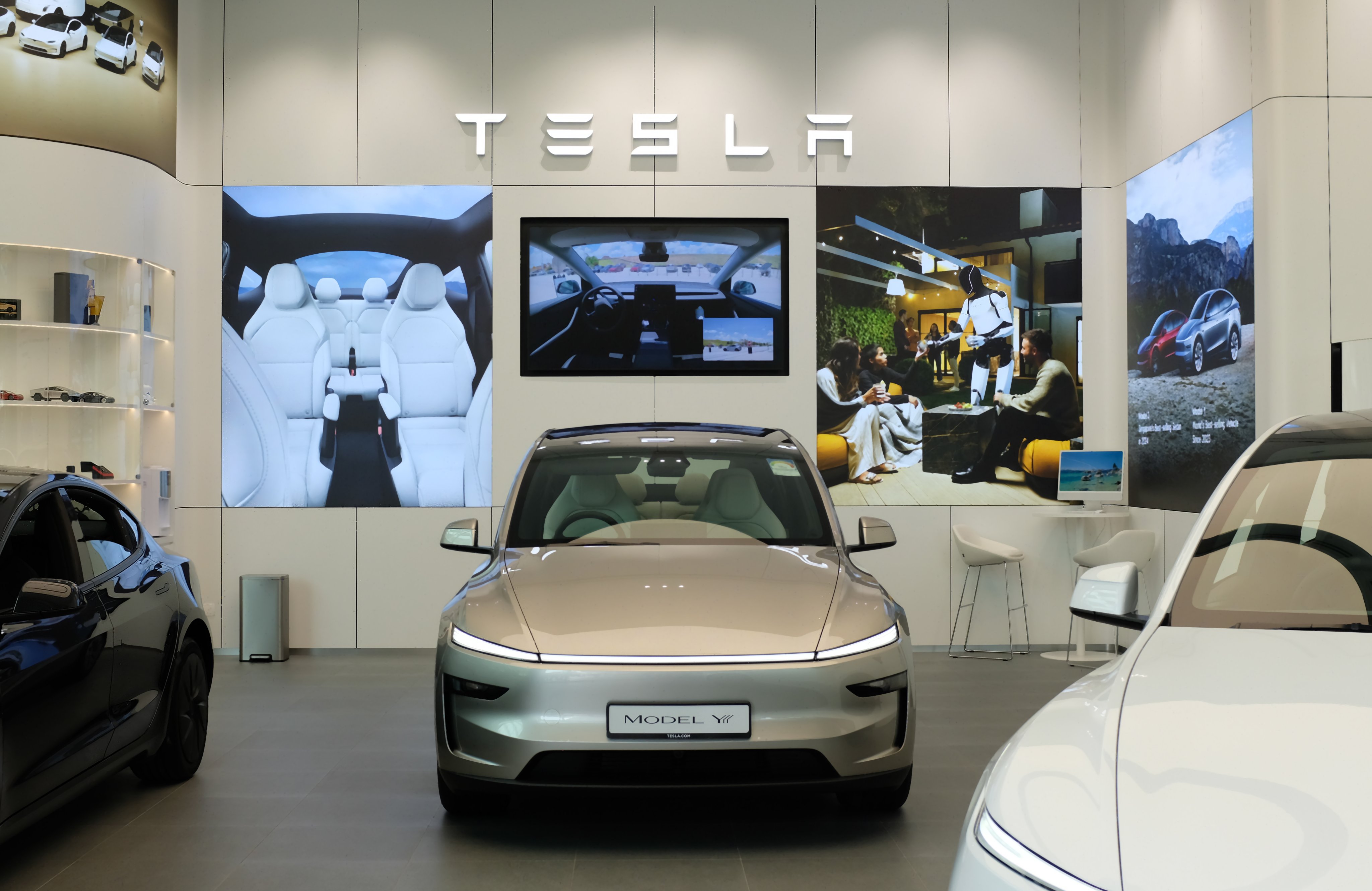 Silver Tesla Model Y on the showroom floor at Bedok Mall, under the TESLA letters, with a Model 3 on the left